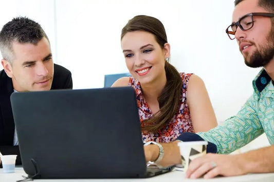 Tre persone che collaborano mentre usano computer convertibili per il lavoro in un ambiente d'ufficio moderno